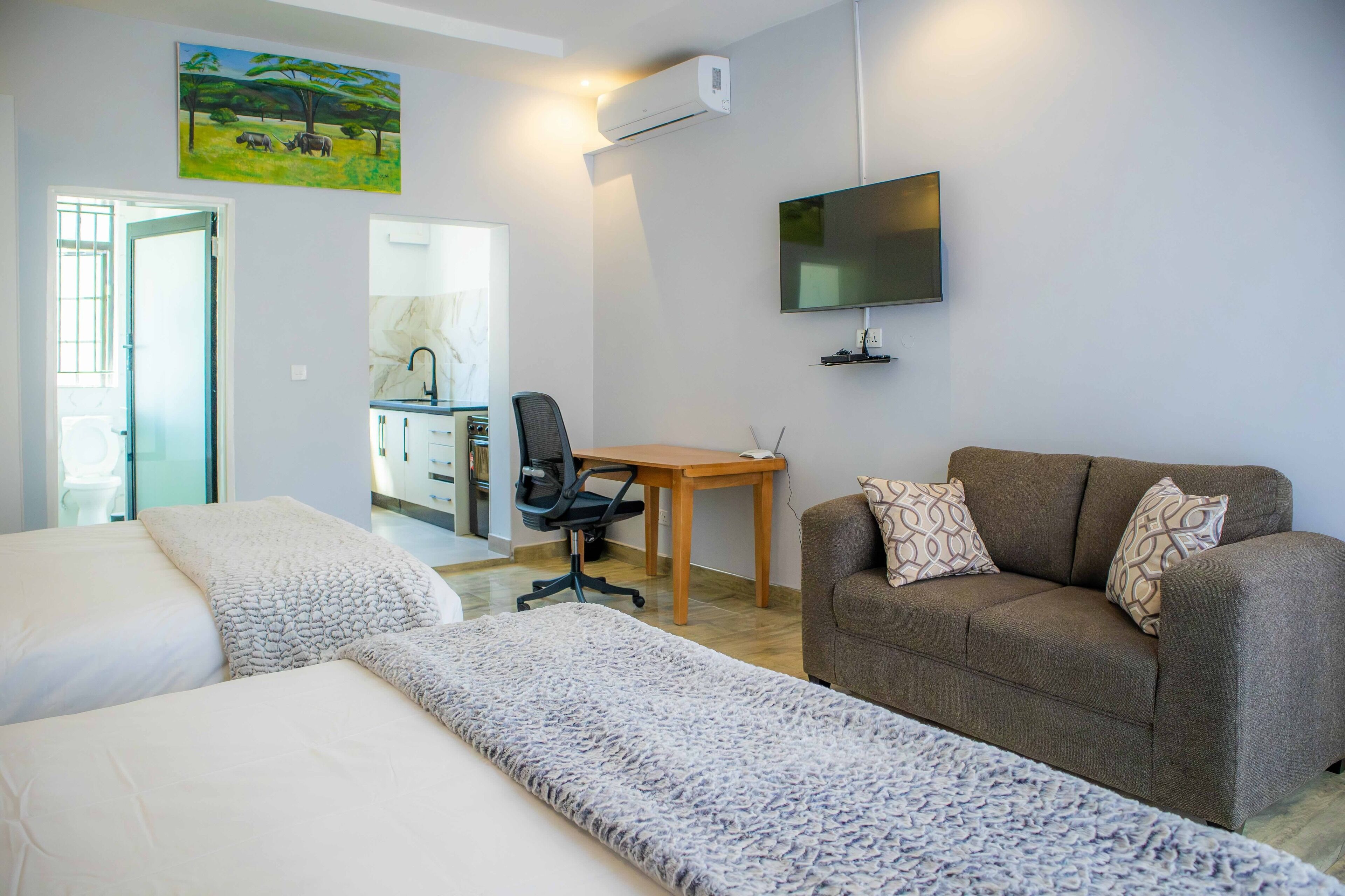 A hotel room with two beds, a sofa, a desk, a chair, and a TV.