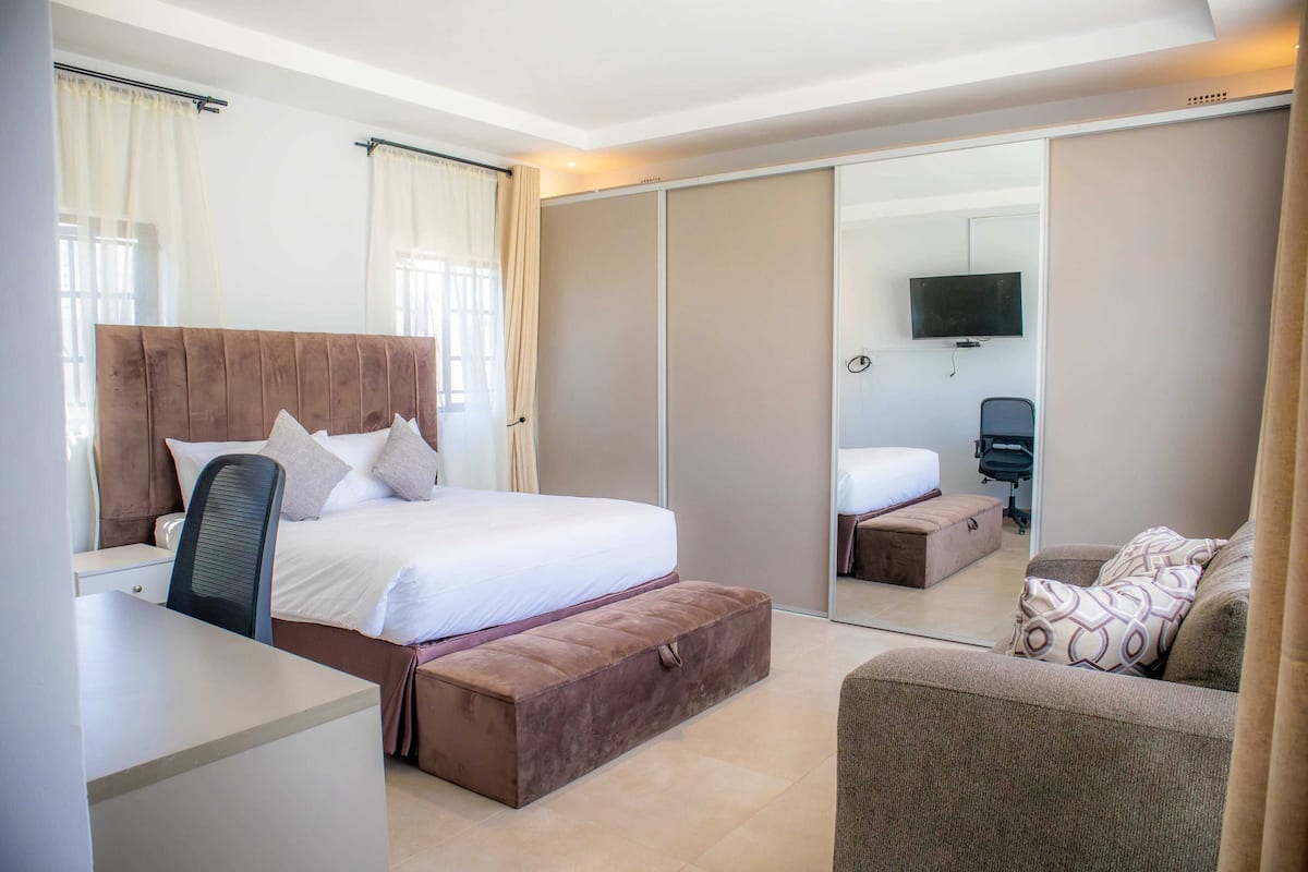 Una habitación de hotel moderna con una cama grande, un escritorio, una silla, un sofá y un espejo.