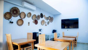 A dining area with wooden tables and chairs, a wall-mounted TV, and a variety of woven plates displayed on the wall.