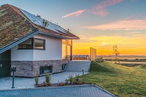 Una casa moderna con tetto spiovente, facciata in pietra e vista sul tramonto sul fiume.