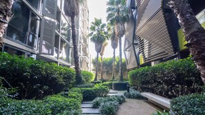 A narrow pathway flanked by lush greenery and modern buildings with large windows and balconies. - Elegant 1-bed Apartment With Premium Amenities (Melbourne)