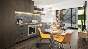 A modern kitchen with dark wood cabinetry, a marble backsplash, and a dining area with a round table and two chairs. - Elegant 1-bed Apartment With Premium Amenities (Melbourne)