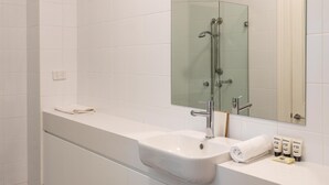 Egy modern fürőszoba fehér csempével borított fallal, üveg zuhanykabinnal, fehér mosdókagylóval, mely felett tükör található, és fekete-fehér kockás mintájú padlóval.