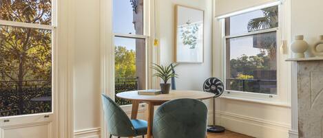 A room with a round wooden table, two chairs, a potted plant, and a framed artwork on the wall.