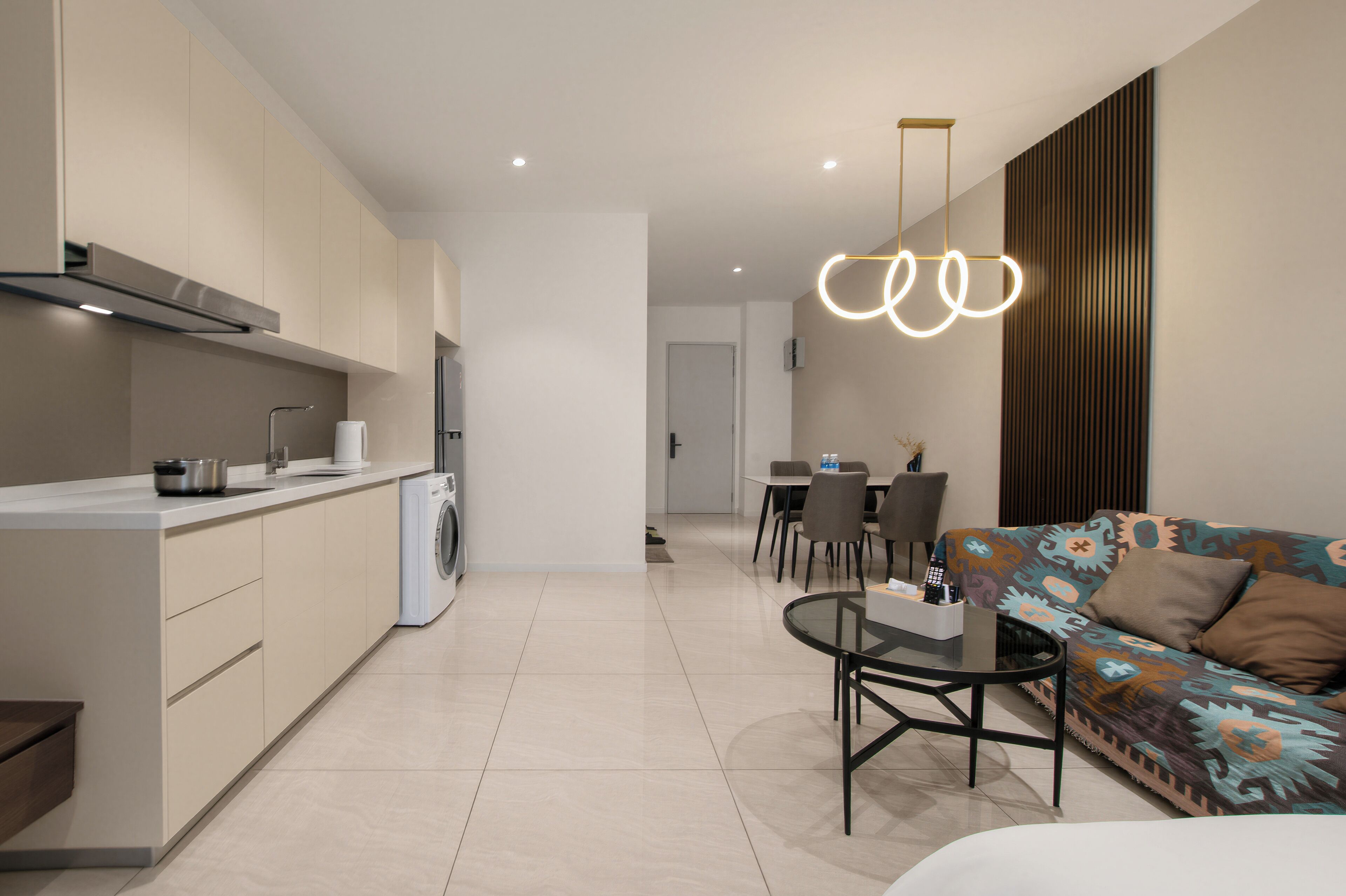 Uma cozinha moderna com máquina de lavar embutida, um espaço de refeições com mesa e cadeiras, e um sofá com almofadas estampadas.