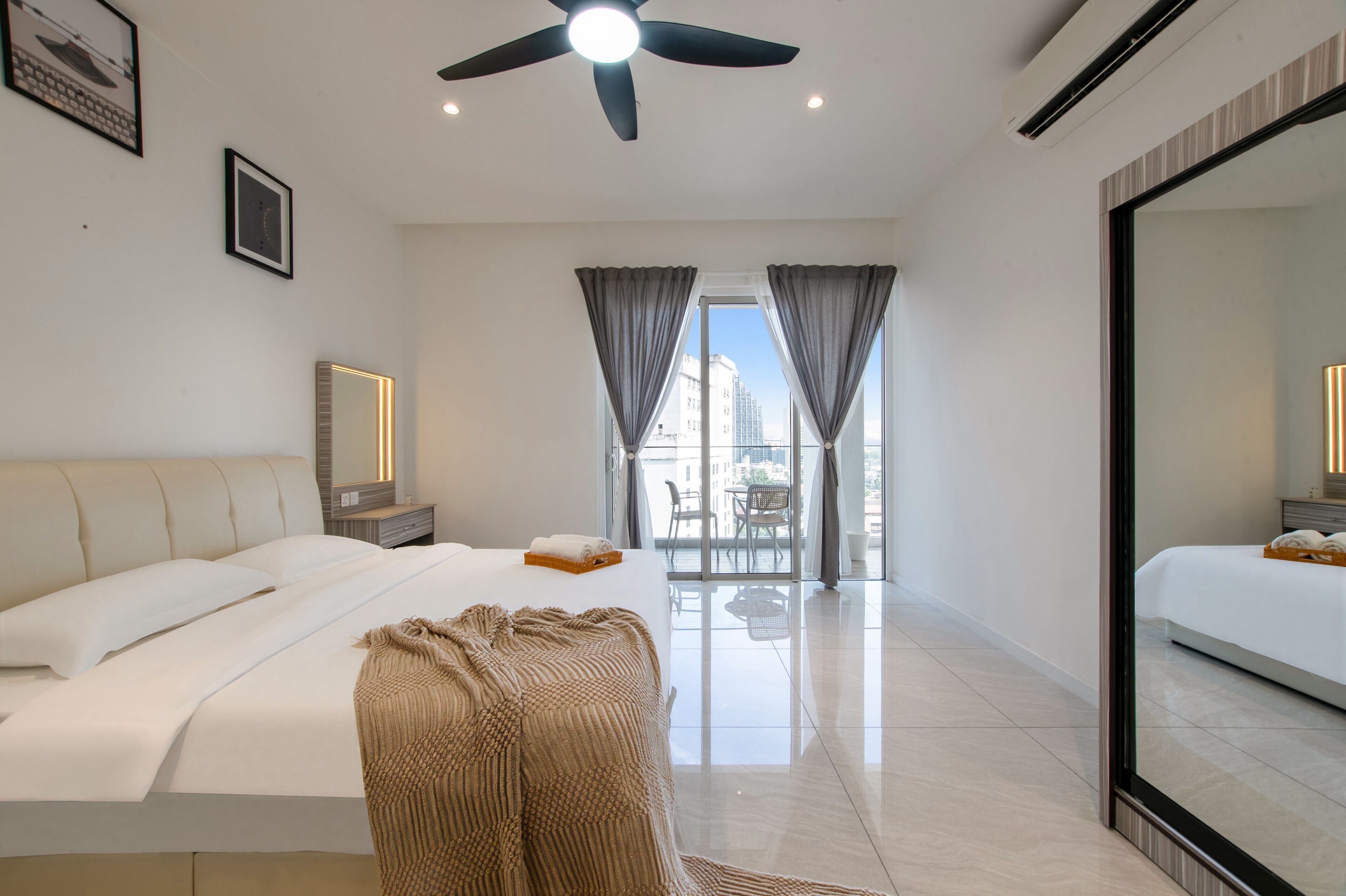 Una habitación de hotel moderna con una cama grande, un ventilador de techo, un balcón con cortinas y un espejo amplio.