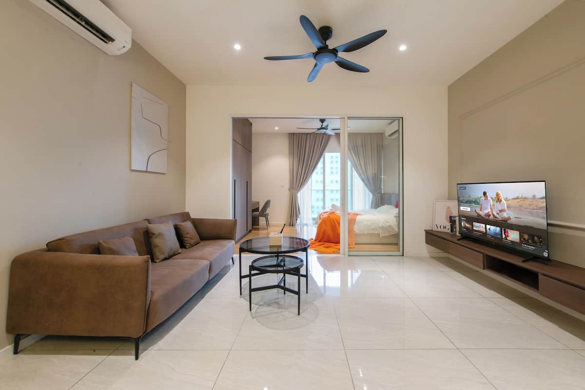 A modern living room with a brown sofa, a glass coffee table, a ceiling fan, and a TV on a wooden stand.