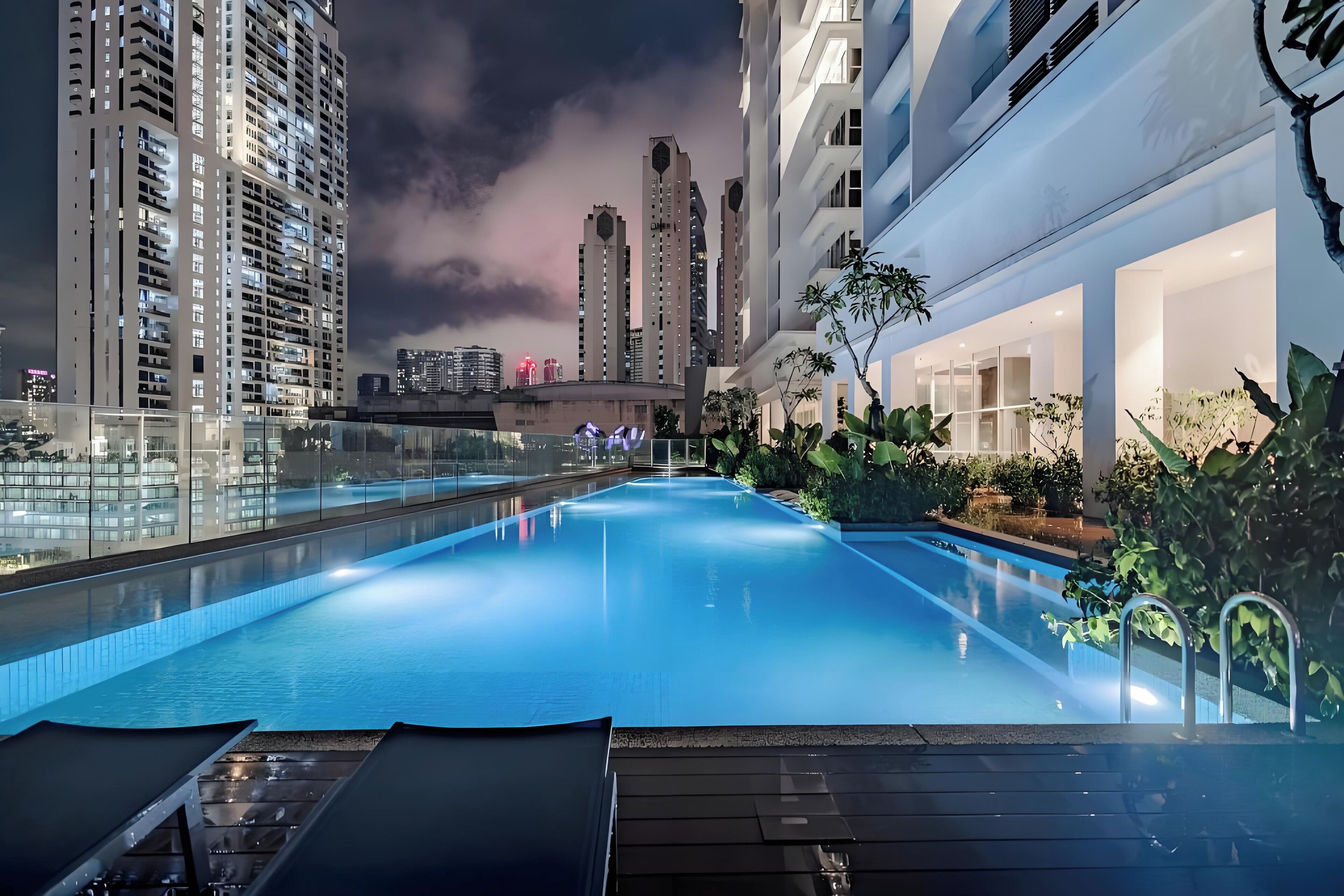 A rooftop pool with glass railings, surrounded by high-rise buildings and lush greenery.