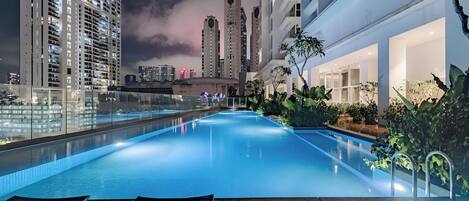 A rooftop pool with glass railings, surrounded by high-rise buildings and lush greenery.