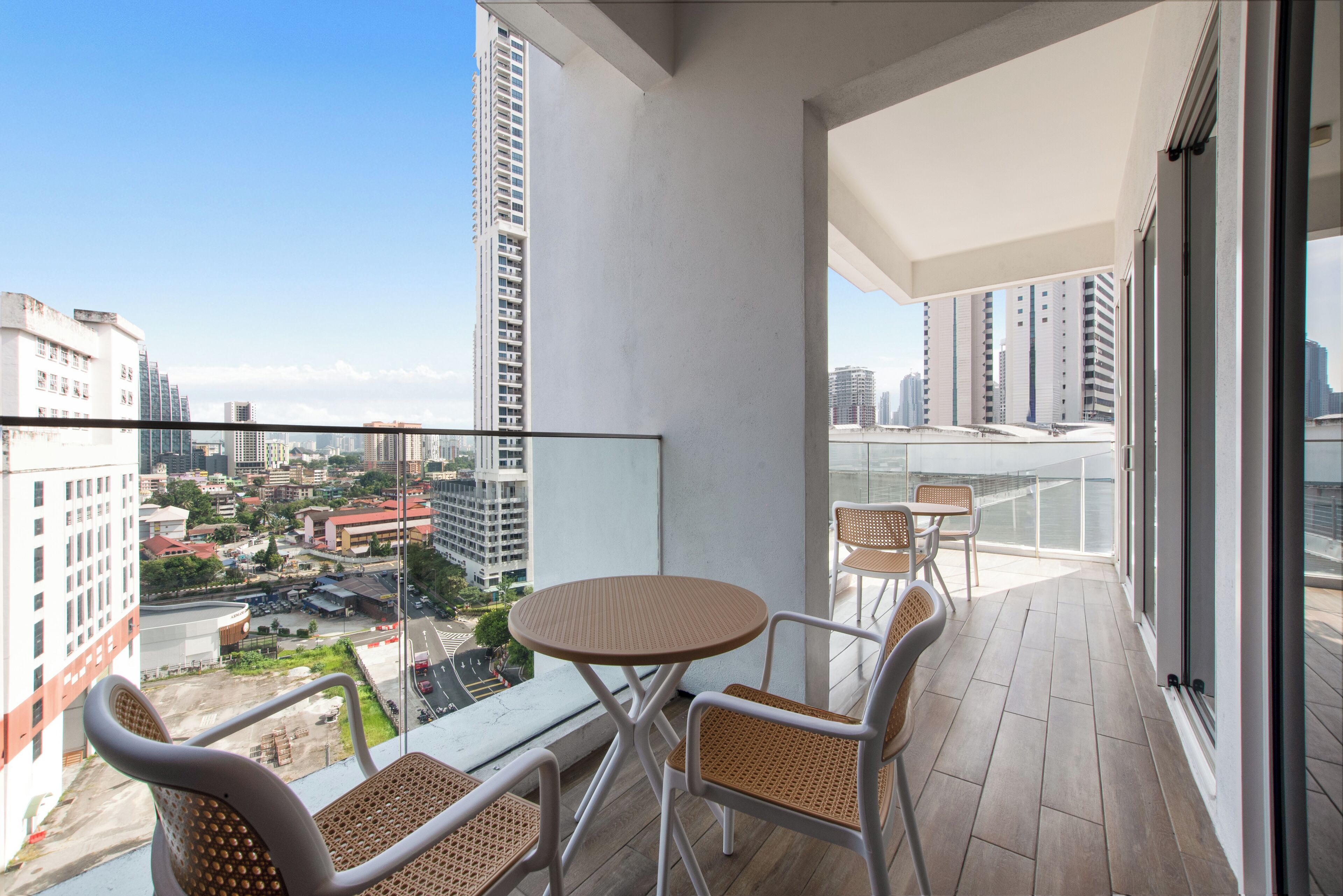 A balcony with a round table and four chairs, overlooking a cityscape with high-rise buildings.