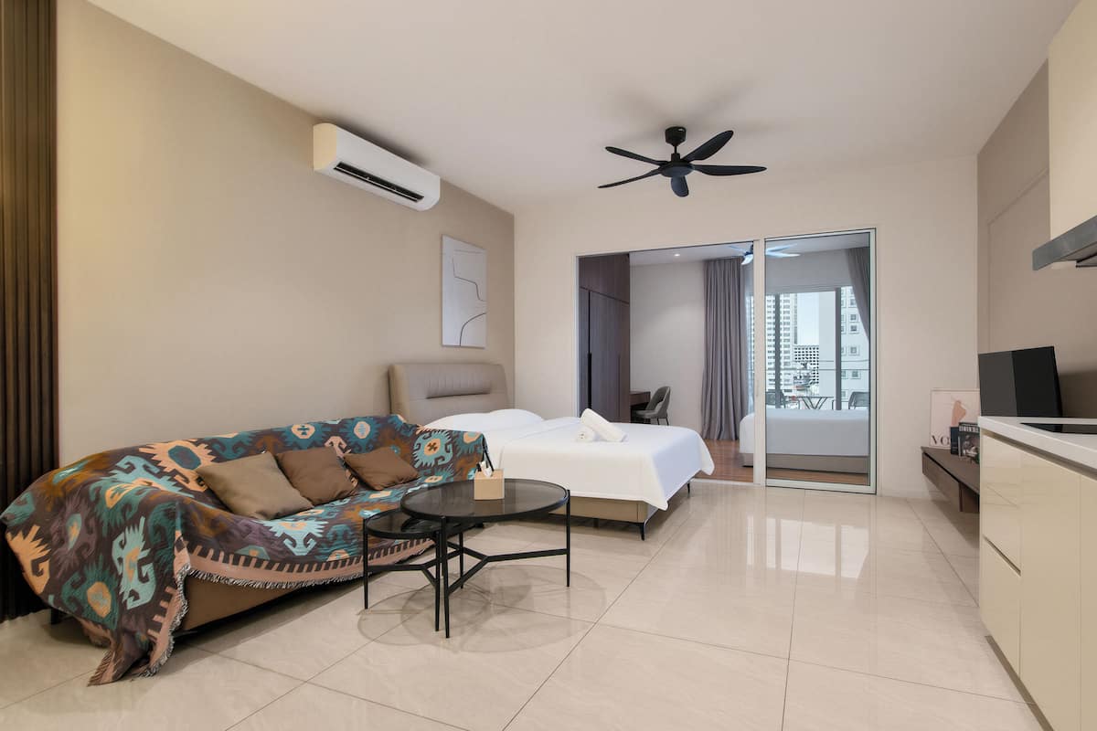 A modern hotel room with a sofa, a bed, a small table, a ceiling fan, and a view through a glass door.
