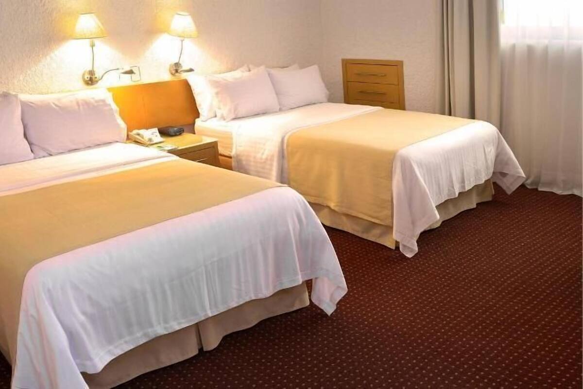Une chambre d’hôtel avec deux lits, une table de chevet, une lampe et une commode en bois.