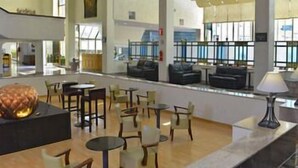 Een ruime lobby met verschillende zithoeken, een receptiebalie en grote ramen die voor natuurlijk licht zorgen.