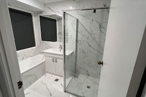 Un baño con ducha acristalada, lavamanos blanco y un espejo grande.