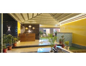 A reception area with a wooden desk, a clock, and a reception desk. There are potted plants and a small garden area. - Hotel Kesar bagh (Chomu)