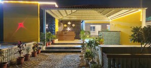 A hotel entrance with a covered walkway, potted plants, and a reception area with a counter and clocks. - Hotel Kesar bagh (Chomu)