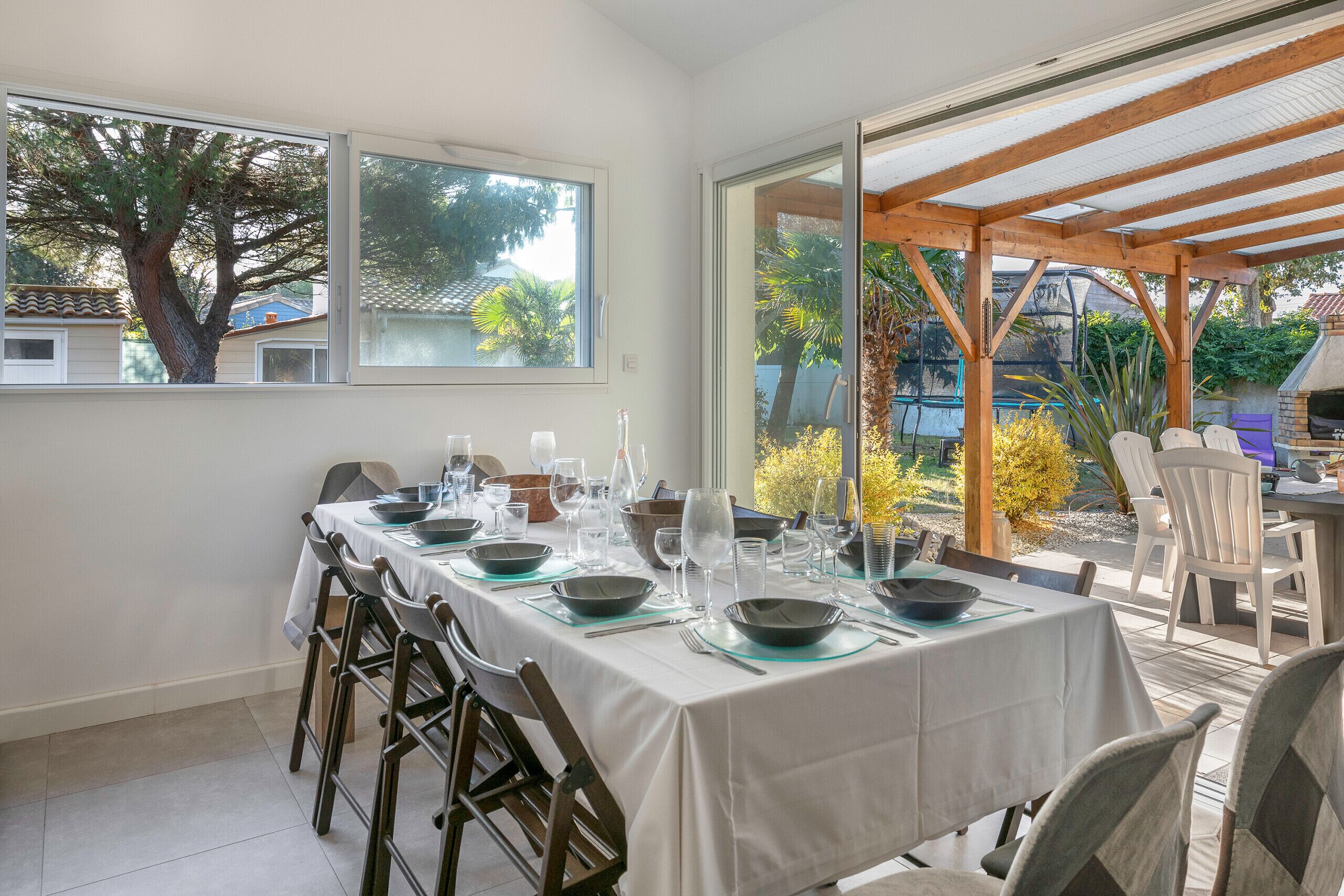 Uma área de refeições com uma mesa posta para quatro pessoas, grandes janelas e vista para o exterior.