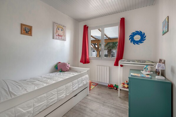 A child's bedroom with a single bed, a desk, and a window with curtains.