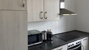 A modern kitchen with light wood cabinets, a black countertop, a built-in microwave, a toaster, and a stove. - Gruppenunterkunft fur 12 Personen in Ballenstedt (Ballenstedt)