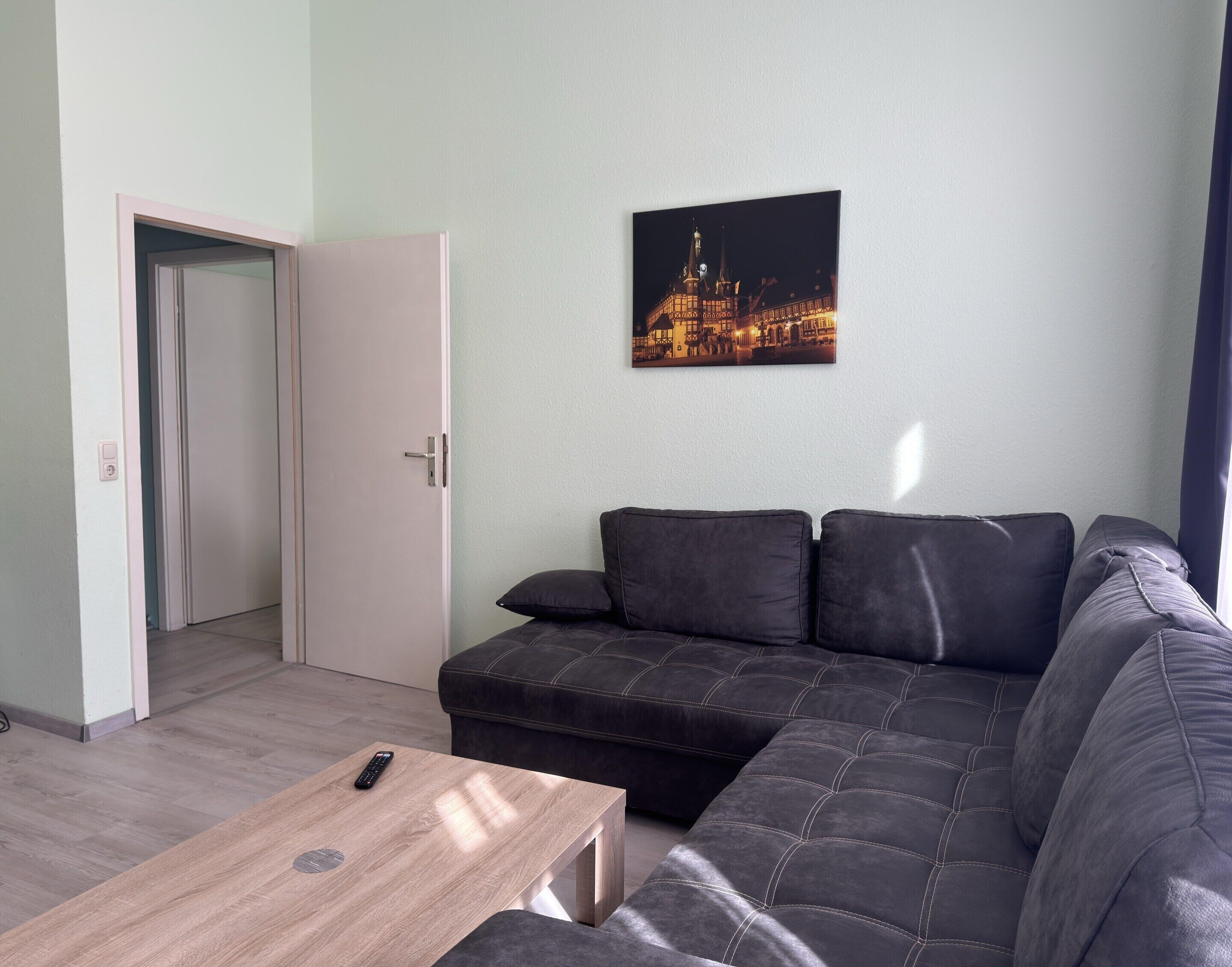 Ett modernt vardagsrum med en hörnsoffa, ett soffbord i trä och en tavla med en stadsbild på väggen.