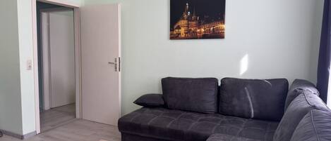 Un salon moderne avec un canapé d’angle, une table basse en bois et un tableau représentant un paysage urbain accroché au mur.