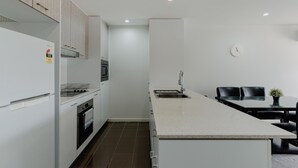 A modern kitchen with white cabinetry, a built-in oven, and a countertop. - Urban 1-bed Apartment in the Heart of the City (Canberra)