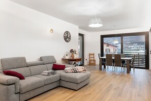 Una sala de estar moderna con un sofá modular, una mesa de comedor con sillas, una lámpara colgante y un ventanal con vistas.