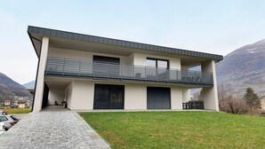 A modern two-story building with a balcony, large windows, and a paved driveway.