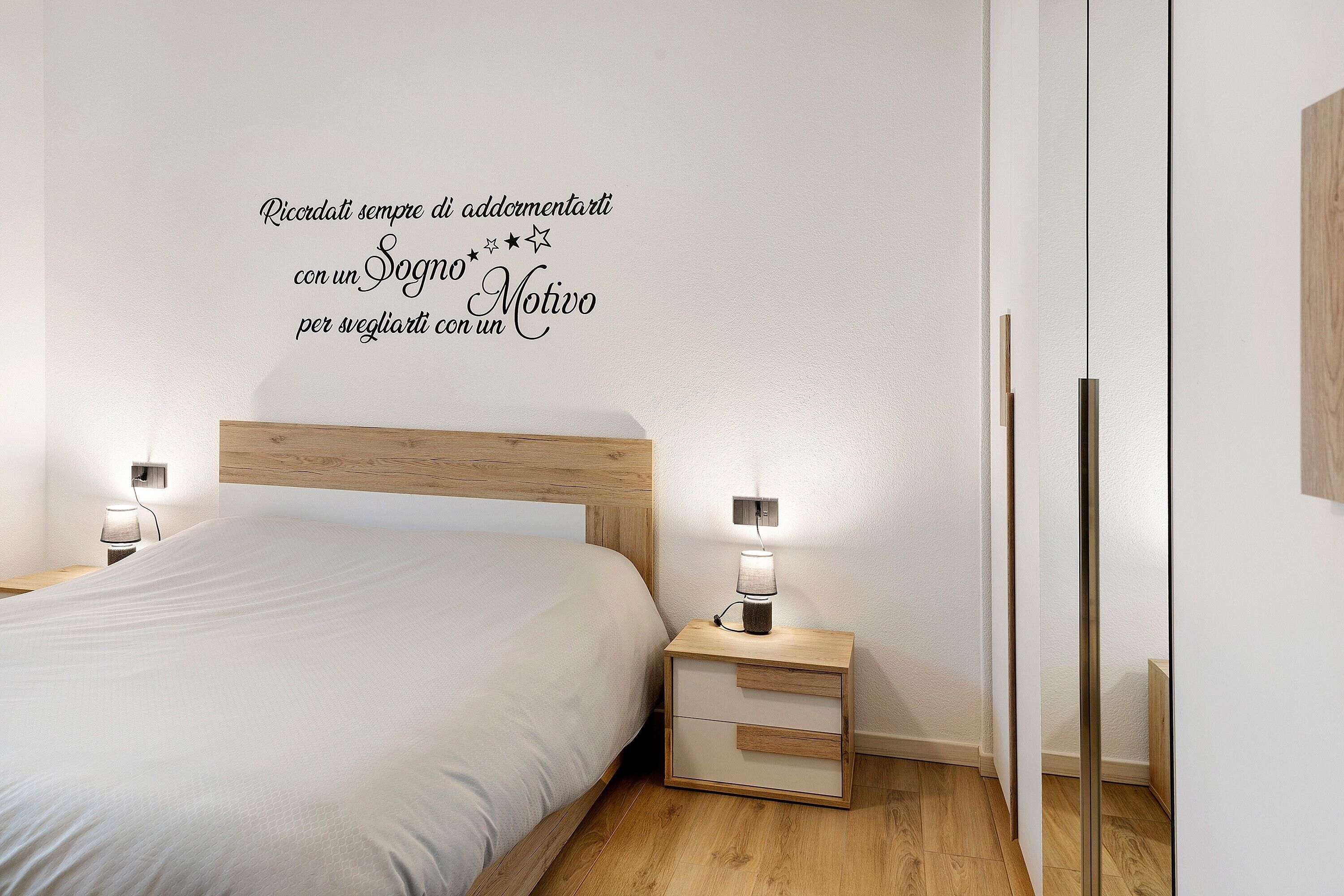 A bedroom with a bed, bedside tables, and a wall with motivational text.