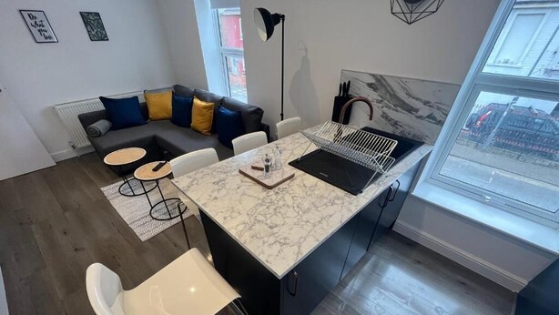 Una cocina moderna con encimera de mármol, pileta integrada y comedor con una silla blanca y una mesita redonda.