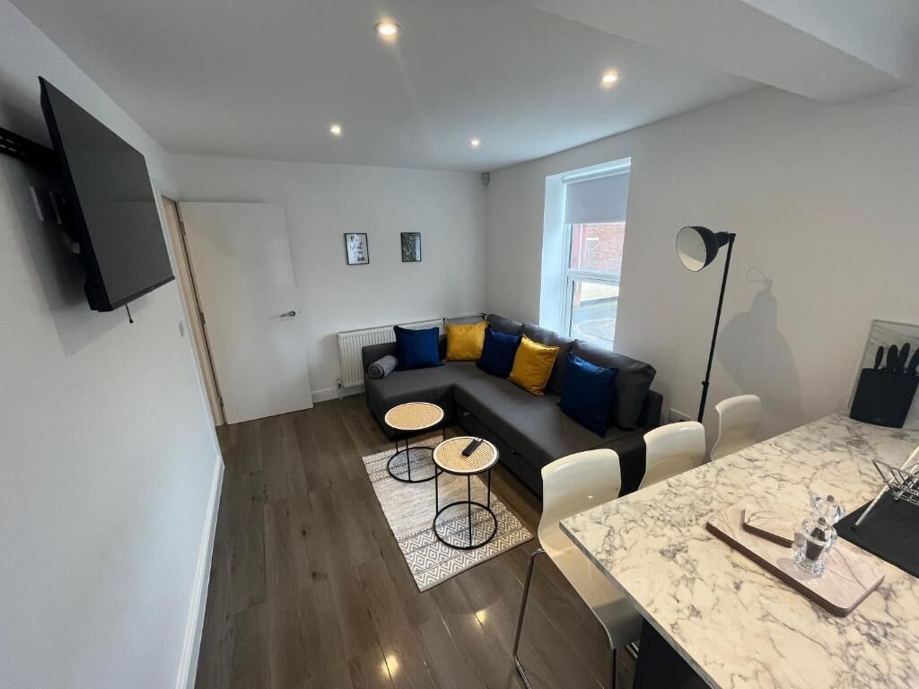 A modern living room with a sectional sofa, a dining table, and a flat-screen TV mounted on the wall.