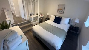 Una habitación de hotel moderna con una cama grande, un vestidor, un escritorio y una mesita con lámpara.