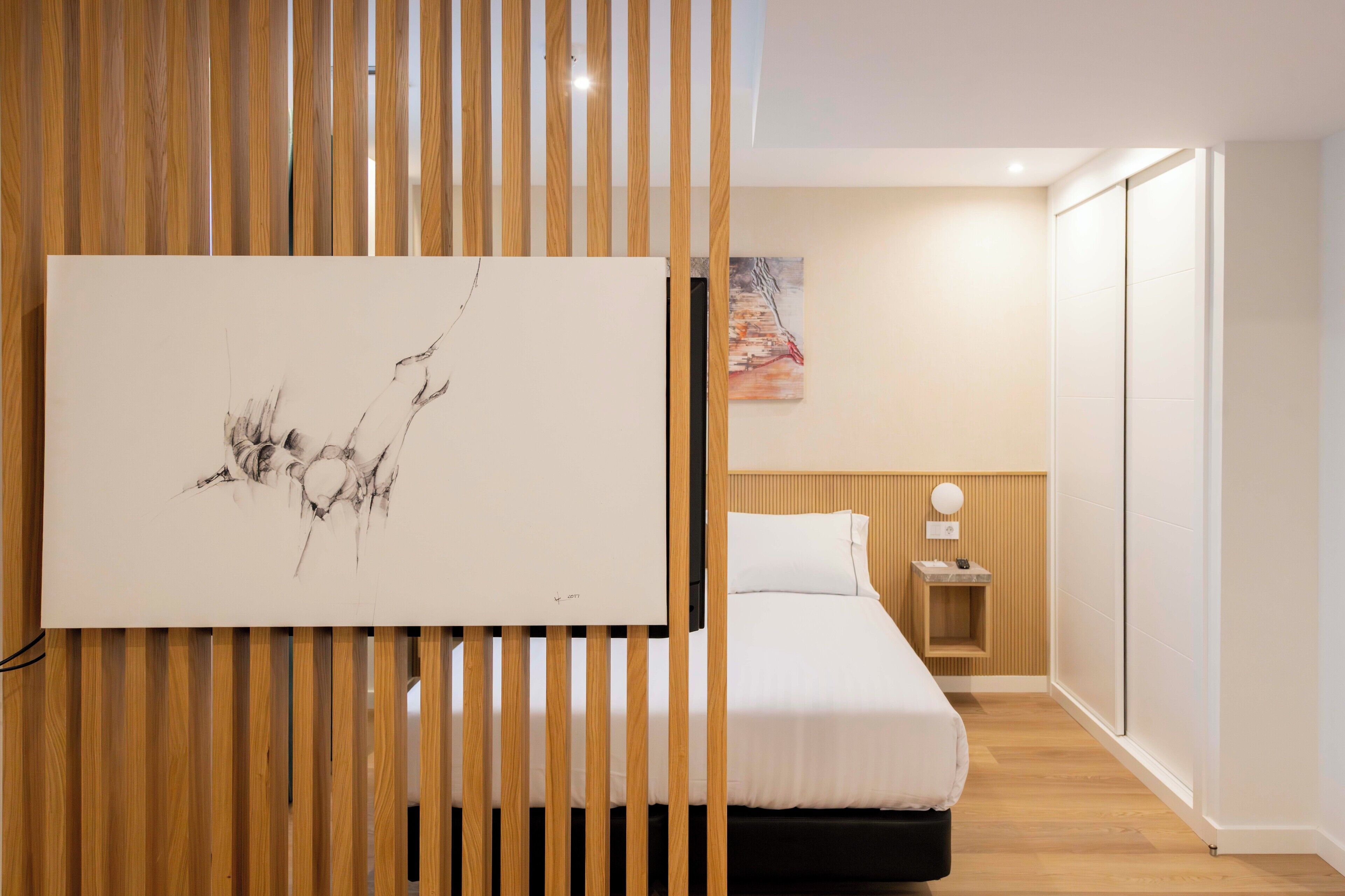 A modern bedroom with a bed, a bedside table, a wall-mounted artwork, and a wooden partition.