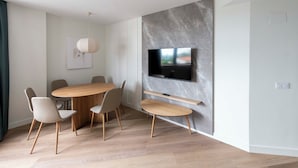 A modern dining area with a wooden table and chairs, a mounted TV, and a marble accent wall. - Apartamentos Silken Goya (Oviedo)