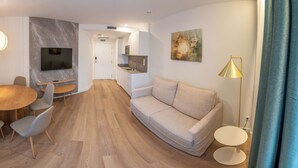 A modern living room with a sofa, a dining table with chairs, a TV mounted on the wall, and a kitchen area in the background. - Apartamentos Silken Goya (Oviedo)