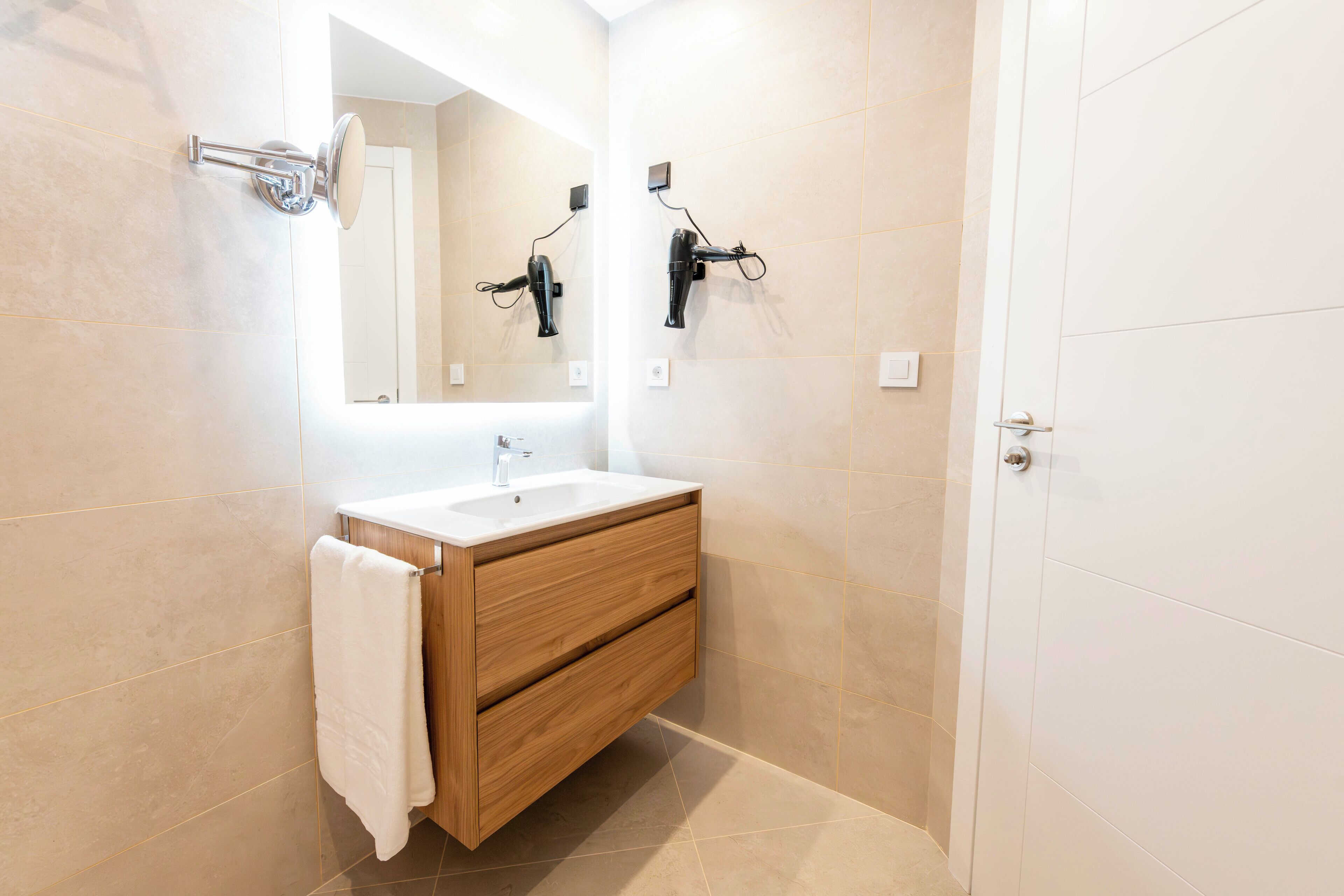Un baño moderno con tocador de madera, un espejo grande y dos secadores de pelo montados en la pared.