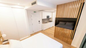 A hotel room with a bed, a TV mounted on the wall, a kitchenette, and a wooden slat partition. - Apartamentos Silken Goya (Oviedo)
