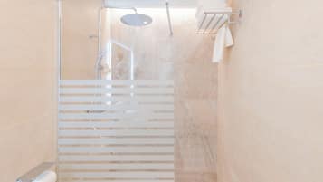 Un baño moderno con ducha envuelta en vidrio, inodoro con un dispensador de toallas de papel y un perchero para toallas.