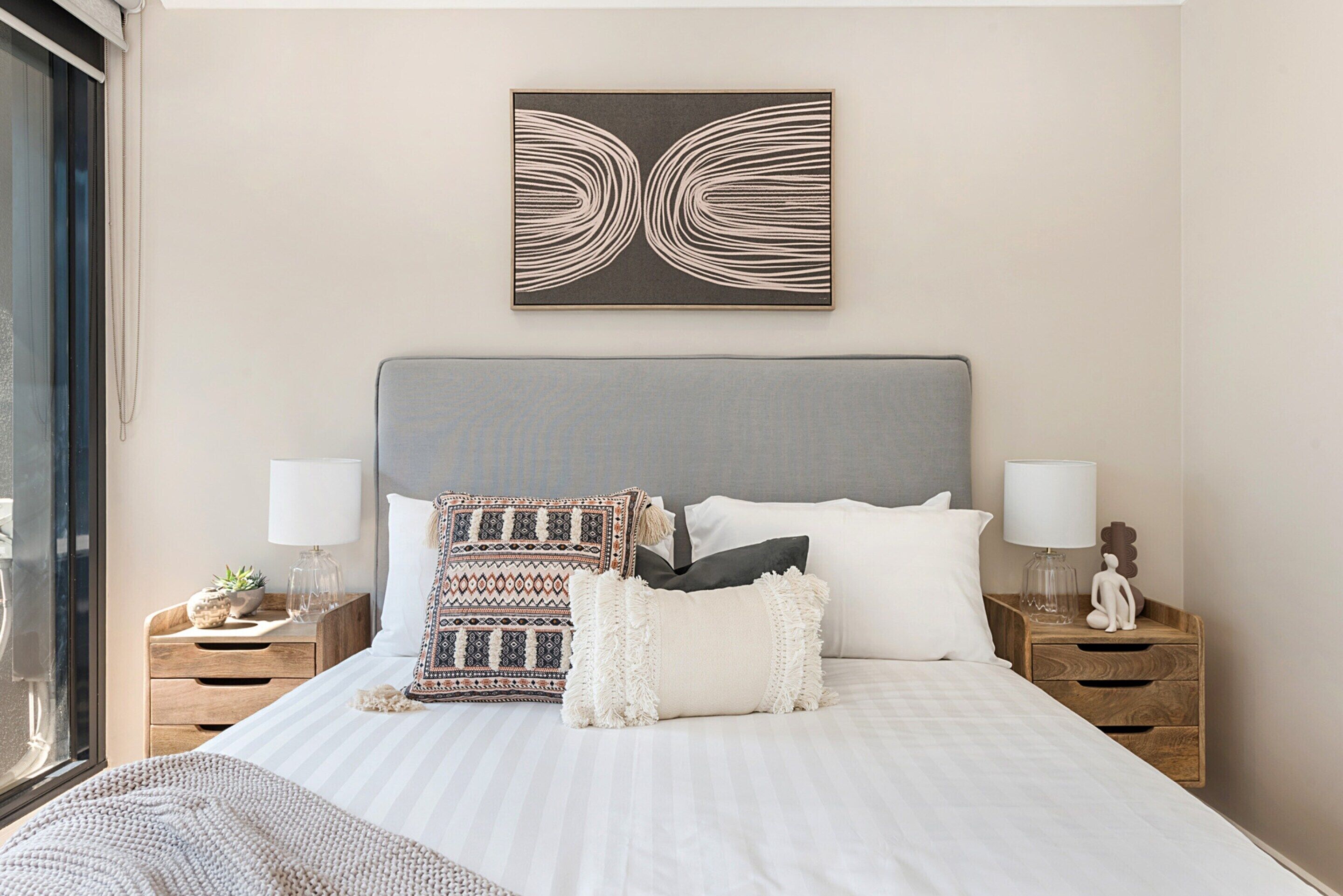 A neatly arranged bedroom with a large bed, two bedside tables, a wall-mounted artwork, and a window.