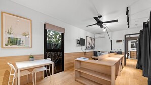 A modern, open-plan living space with a dining area, a kitchen, and a large window. - Stylish New Farm Apartment With Courtyard (Brisbane)