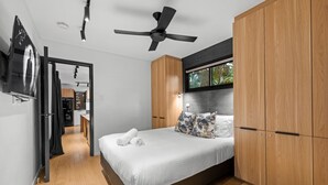 A modern bedroom with a bed, wooden wardrobe, ceiling fan, and a TV mounted on the wall. - Stylish New Farm Apartment With Courtyard (Brisbane)