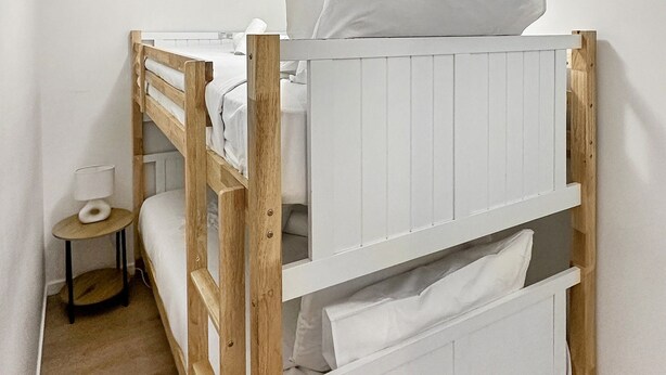 Un letto a castello con biancheria bianca e un comodino con una lampada.