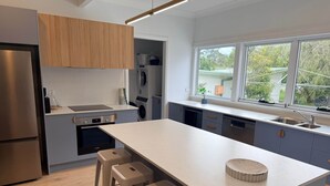 Une cuisine moderne dotée d’un îlot central, de tabourets de bar, d’un four encastré et d’une fenêtre offrant une vue sur l’extérieur.