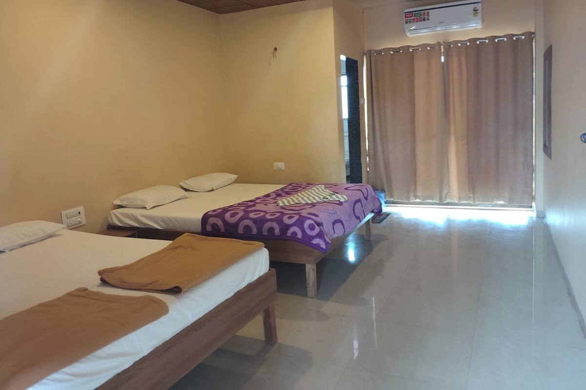 A hotel room with two beds, a window with curtains, and an air conditioning unit.
