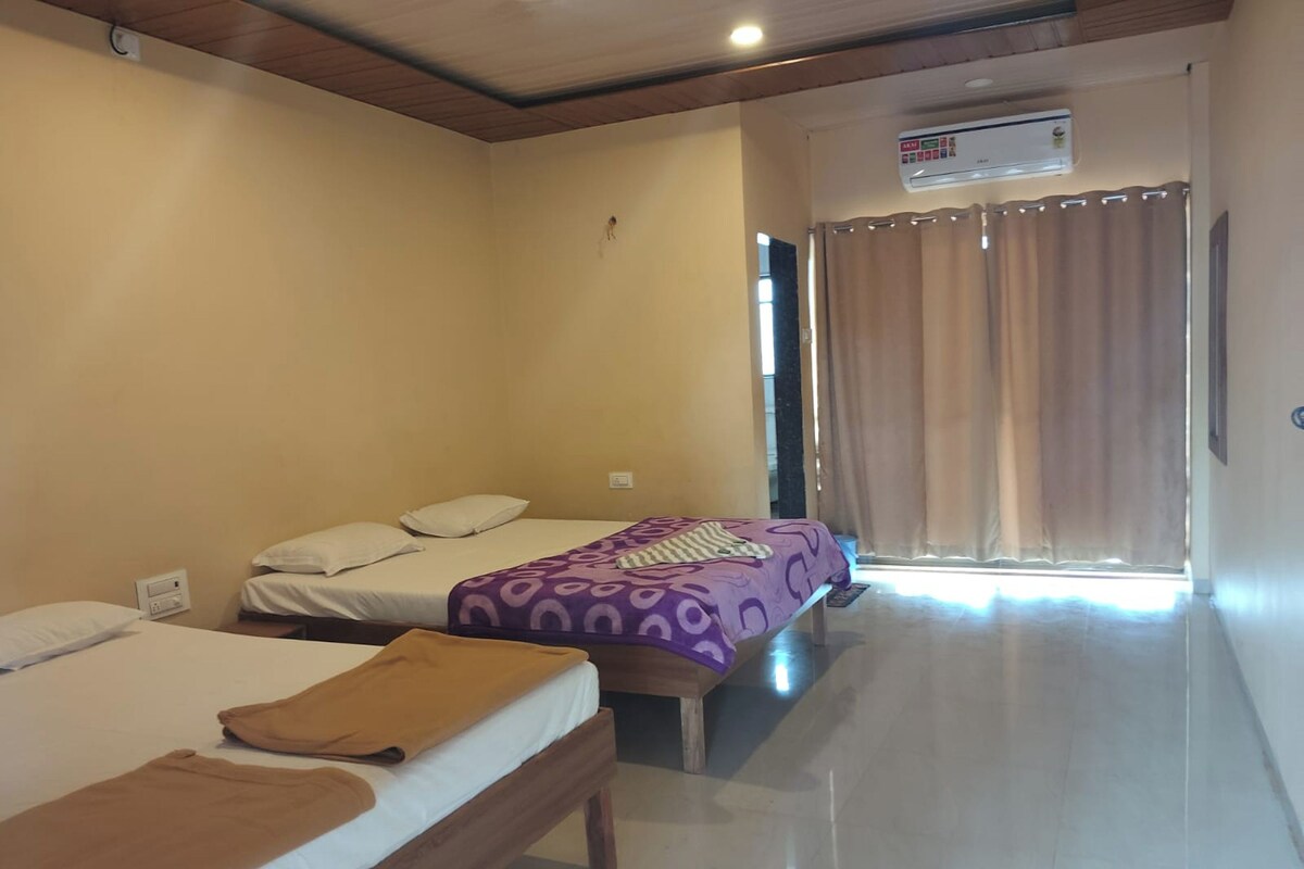 A hotel room with two beds, a wooden ceiling, an air conditioning unit, and a view of the outside through a window with curtains.