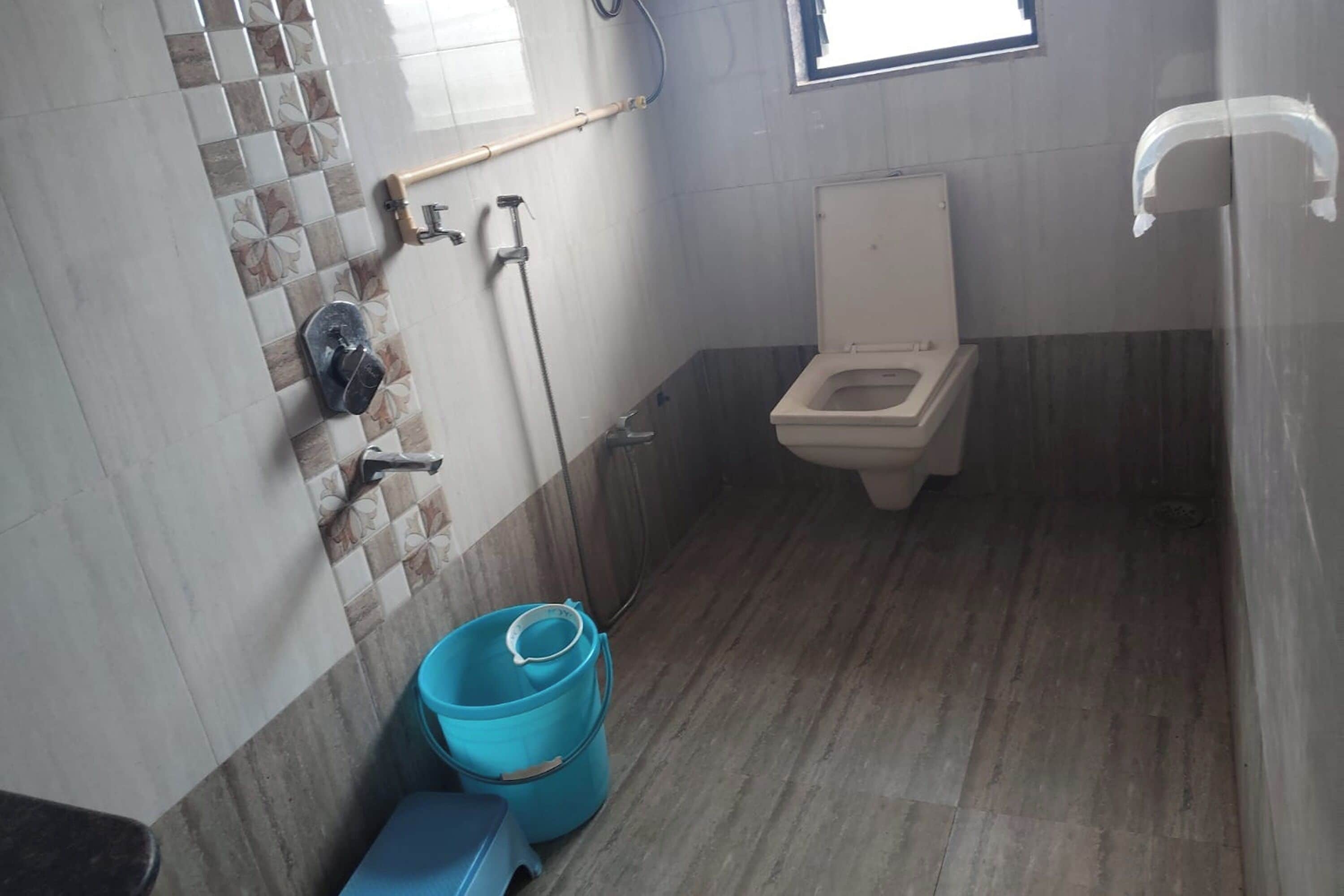 A small bathroom with a toilet, a blue bucket, and a hand dryer.
