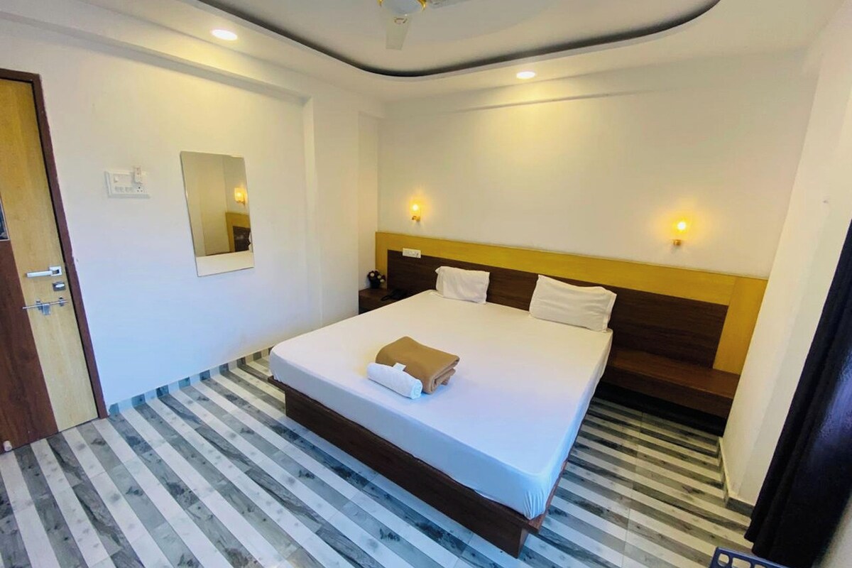 A hotel room with a large bed, wooden headboard, two bedside tables, a mirror, and a striped floor.