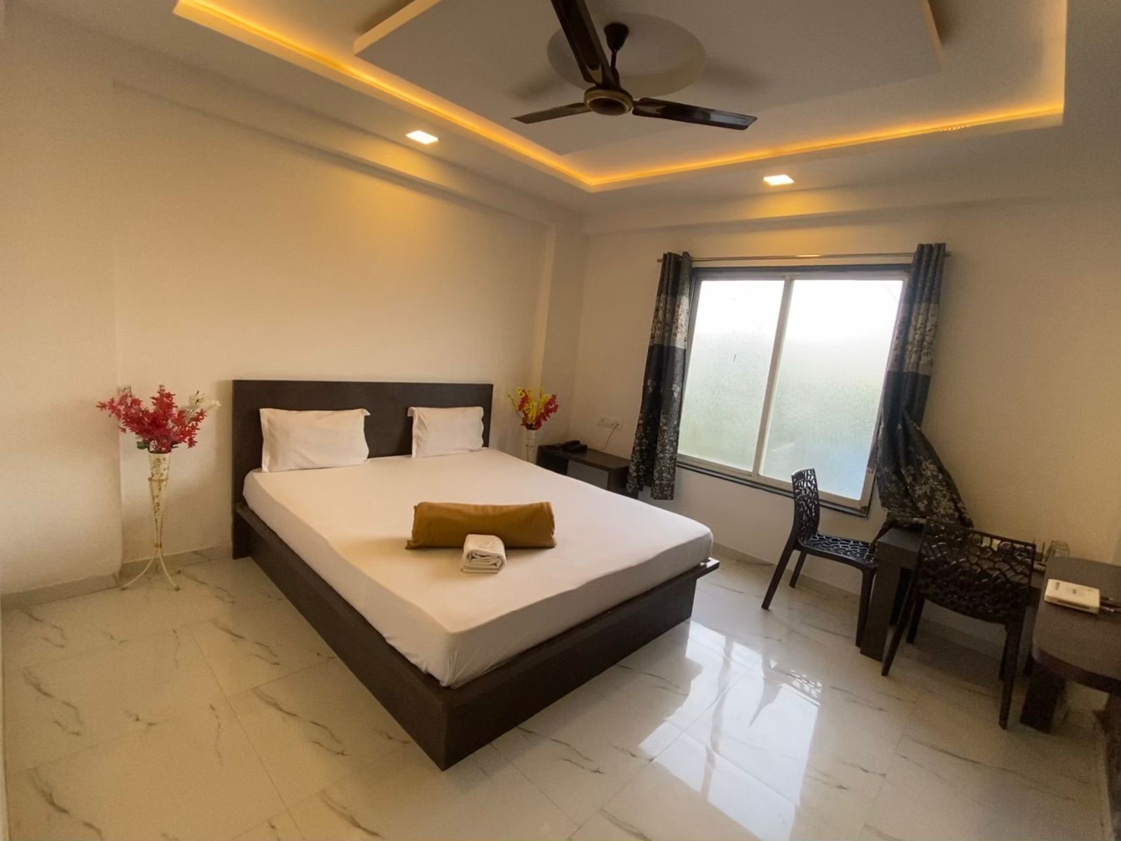 A hotel room with a bed, a desk, a chair, a ceiling fan, and a window with curtains.