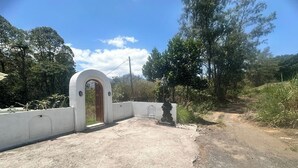 A concrete pathway leading to a white-walled building with a wooden door. - Felysia Villa III (Kintamani)