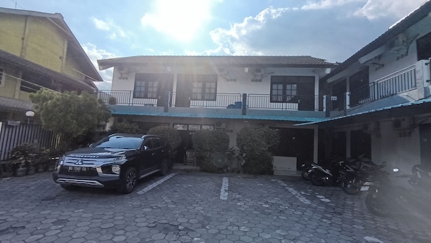 A building with a tiled roof, a black car parked in front, and several motorcycles parked nearby. - Jj House Kost Exclusive Nologaten (Depok)